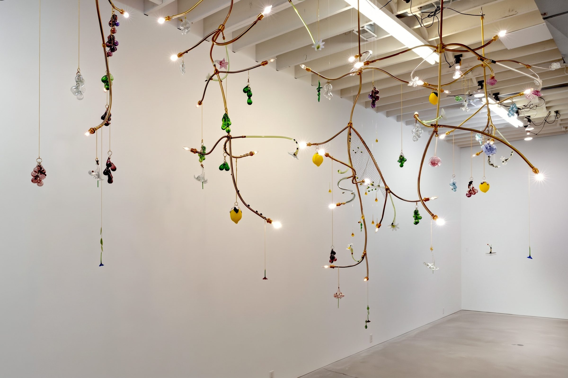 Several Gardening chandeliers of bent brass and glass fruit hanging together in a white gallery